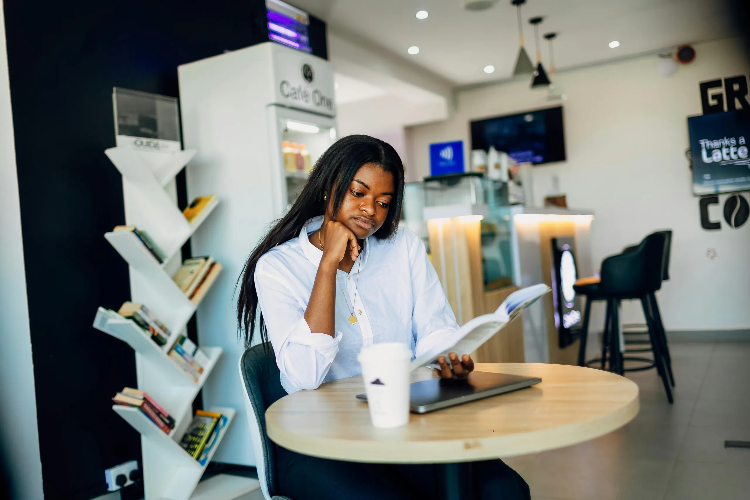 Young professional appearing overwhelmed while reading at a café, symbolizing a solo virtual assistant juggling multiple responsibilities.