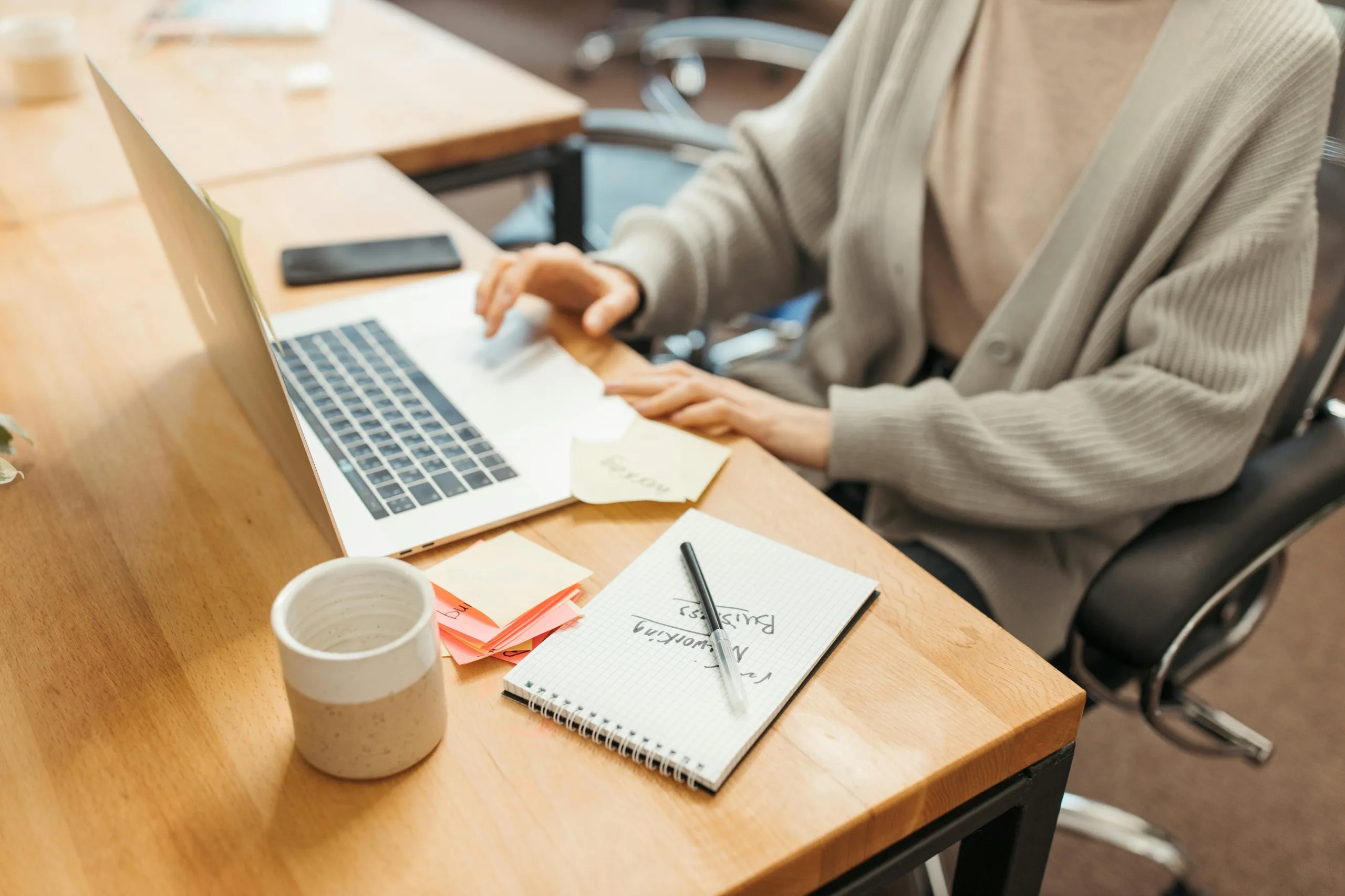 Focused woman using a laptop at a tidy desk with sticky notes, representing a virtual executive assistant managing tasks.