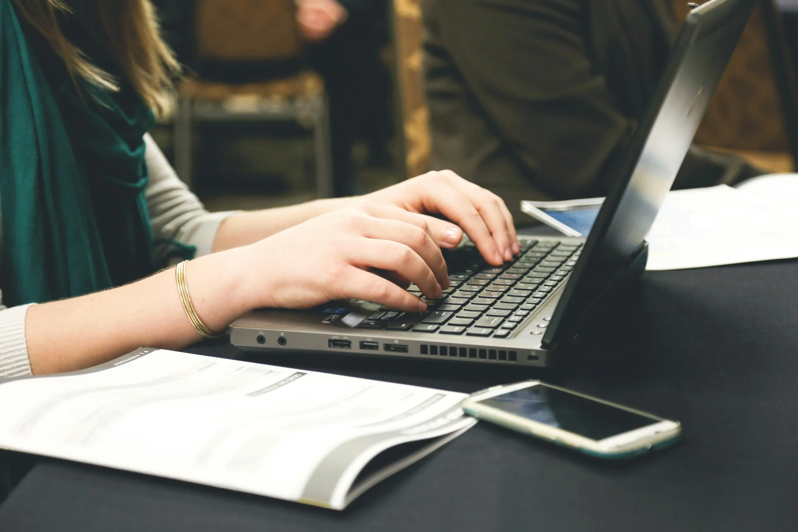 Person typing on a laptop with documents and a smartphone nearby, focused on lead generation research.