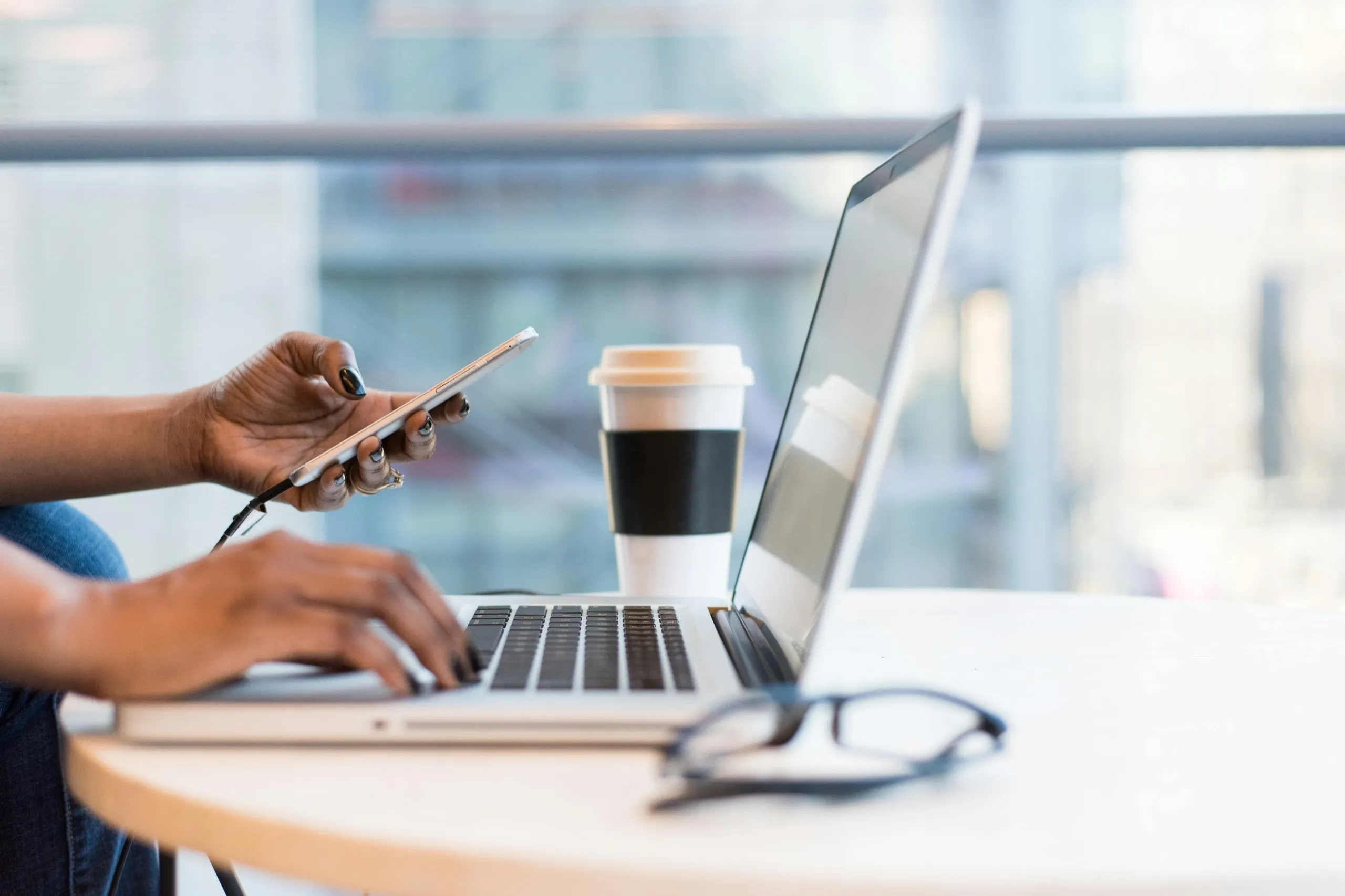 Person working on laptop and smartphone with coffee cup on desk, representing digital lead generation activities.