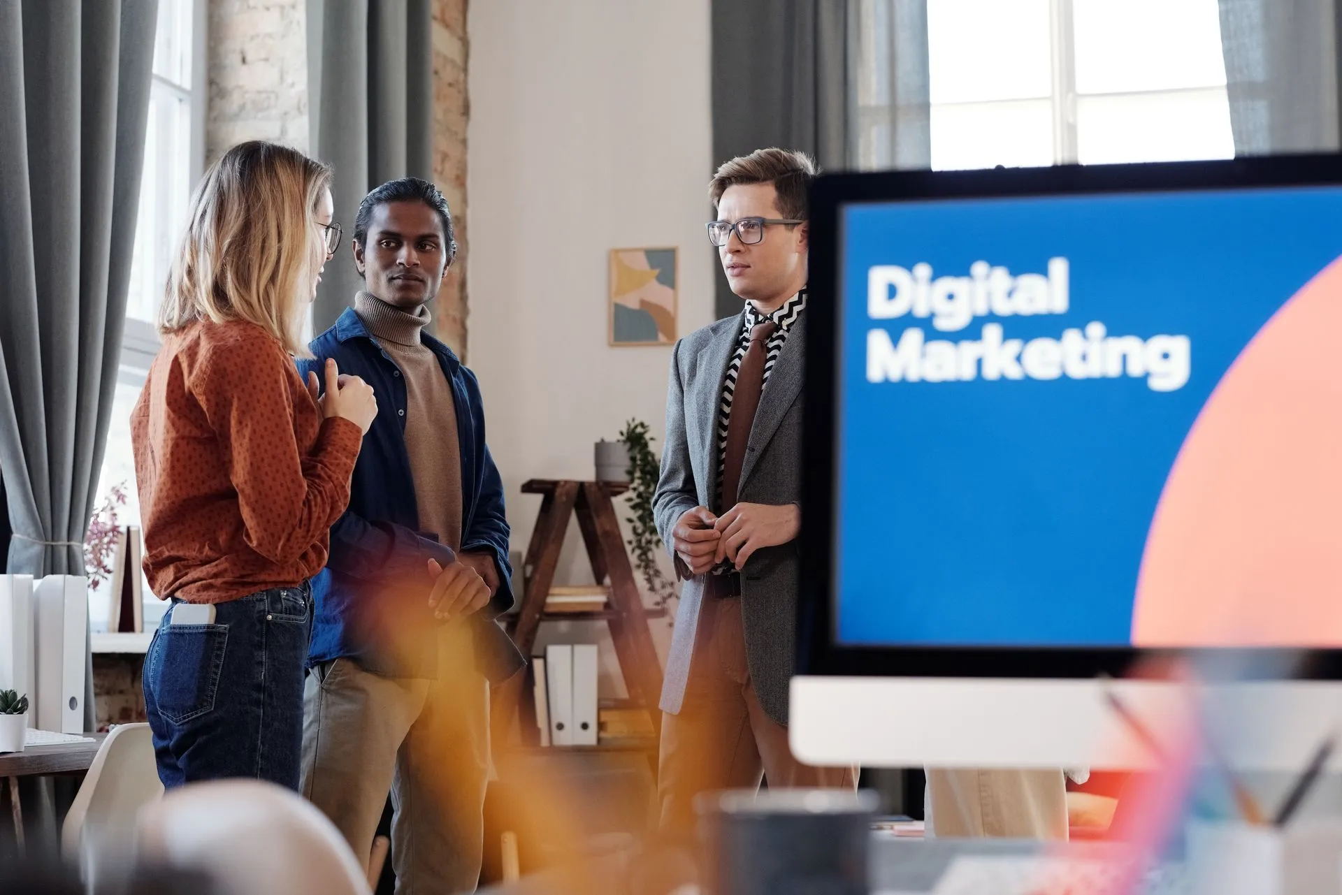 Digital marketing team discussing SEO strategy in an office with a digital marketing presentation on a monitor.